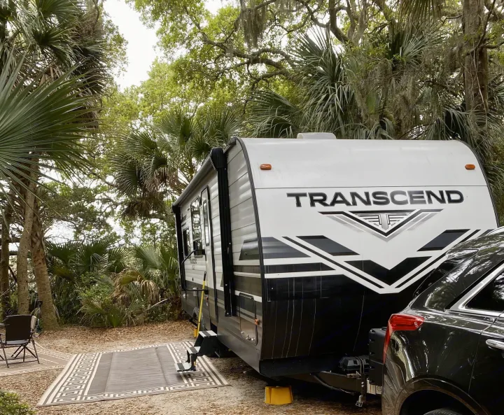 Enjoying our rv rental at a lush, tropical campsite. A Transcend travel trailer is hitched to an SUV, ready for adventure.. Grand Design Transcend Xplor 2021