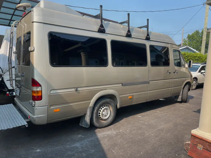 Explore with this beige Sprinter camper van RV rental, equipped with a roof rack, rear ladder, and ramp for easy loading.. Mercedes Sprinter 2006