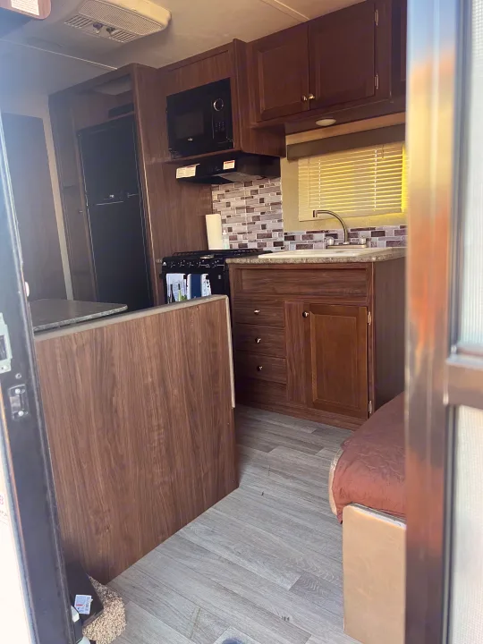 Inside this **rv rental**, discover a well-equipped kitchen with dark wood cabinets, a stove, sink, microwave, and fridge, plus a brown seating area.. Dutchmen Coleman Lantern LT 2016