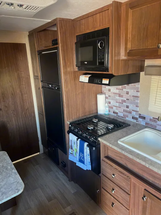 rv rental kitchen featuring a microwave, stove, sink, and refrigerator, all framed by warm wood-look cabinetry.. Dutchmen Coleman Lantern LT 2016