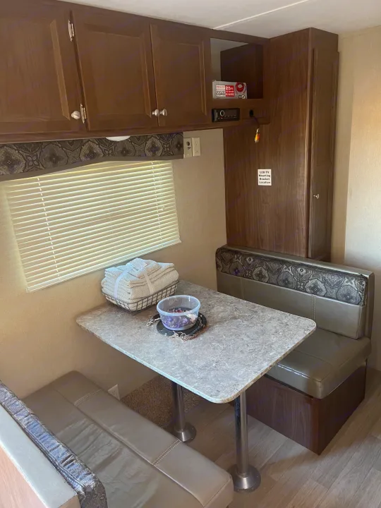 Cozy RV rental dinette features a table, cushioned benches, overhead cabinets, and an LCD TV mounting area.. Dutchmen Coleman Lantern LT 2016