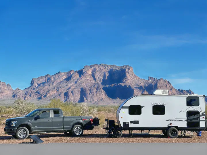 Grey Ford F-150 truck and Wolf Pup RV rental trailer parked with a mountain backdrop in a vast desert landscape.. Forest River Cherokee Wolf Pup Black Label 2021