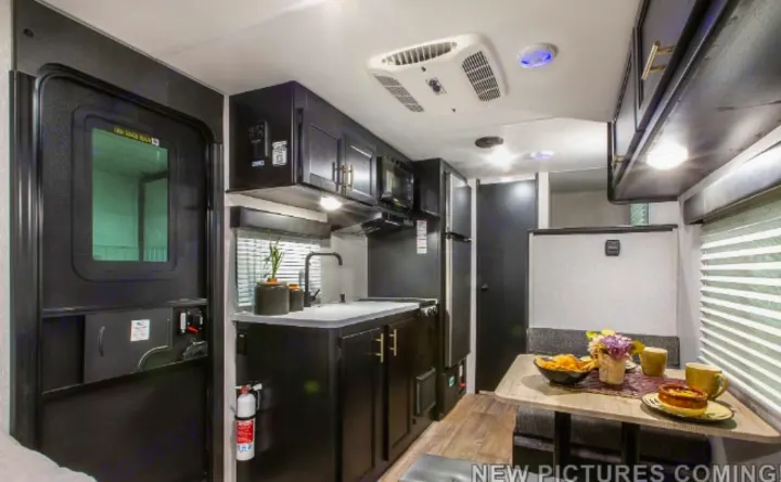 Modern RV rental interior: dark-cabinet kitchen with fridge & microwave, plus a cozy dinette. Ready for your adventure.. Forest River Cherokee Wolf Pup Black Label 2021