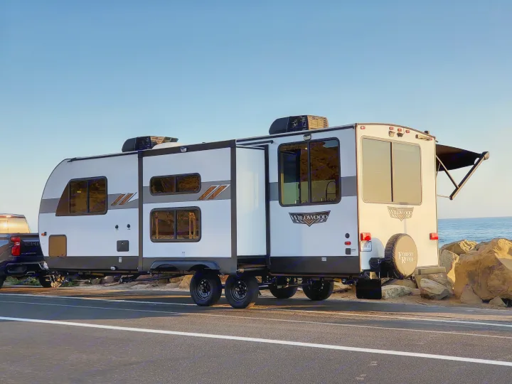 A white Wildwood Forest River travel trailer, perfect as an RV rental, parked ocean-side with slide-outs extended for adventure.. Forest River Wildwood 24 view 2024