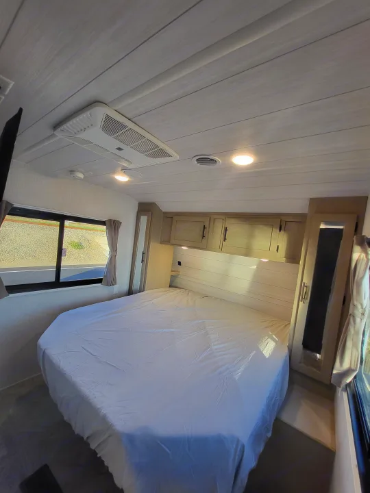 Bright RV rental bedroom featuring a comfortable bed, paneled ceiling, overhead AC, and storage. Ideal for travelers.. Forest River Wildwood 24 view 2024