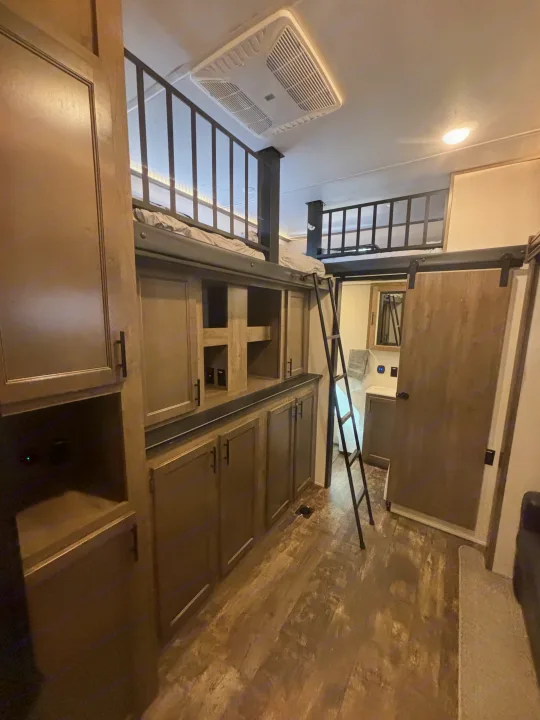 RV rental interior: A wooden loft bed with a ladder overlooks built-in storage. A barn door slides to reveal the bathroom.. Forest River Sabre 2022