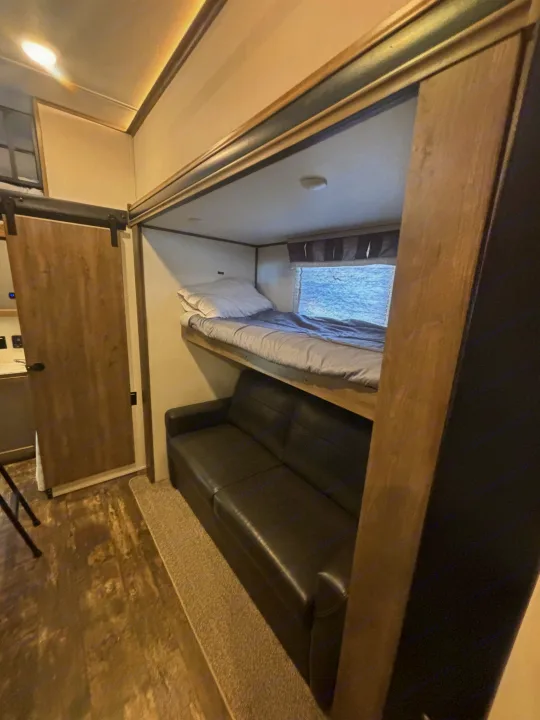 An RV rental interior featuring a practical bunk bed over a black sofa, with a sliding door on the left.. Forest River Sabre 2022
