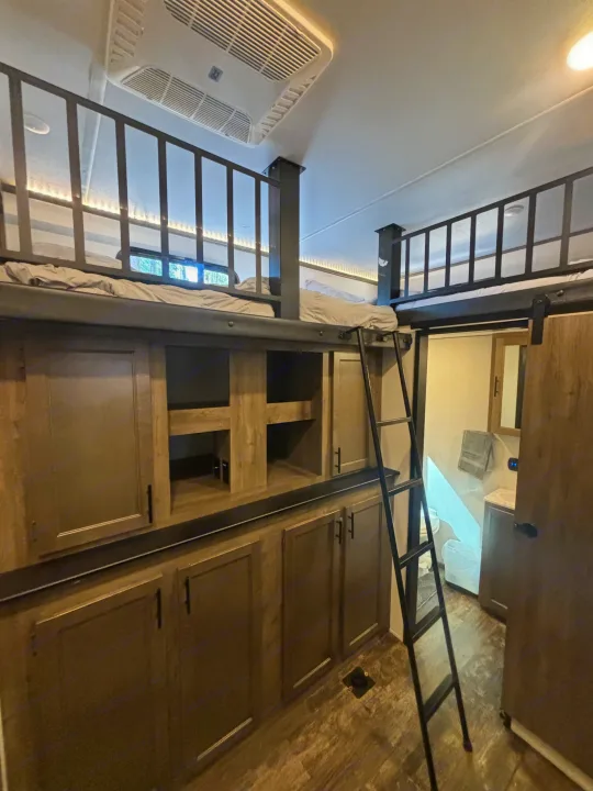 RV rental interior features a bunkhouse with two upper beds, ladder, ample wood cabinetry, and a visible bathroom.. Forest River Sabre 2022