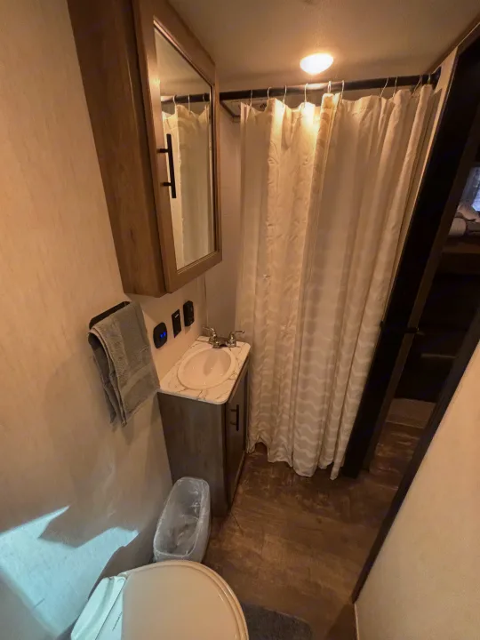 This RV rental features a compact bathroom, including a shower with curtain, sink vanity, mirror, and toilet, maximizing space.. Forest River Sabre 2022