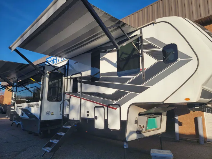 A large white Momentum M-Class fifth-wheel RV, with multiple awnings extended, ready for your next rv rental adventure.. Grand Design Momentum 2022