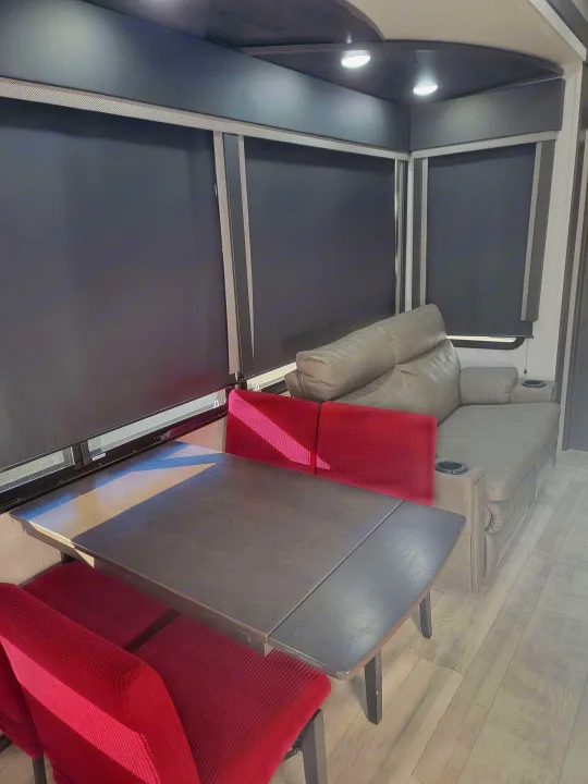 RV rental interior featuring a dark dining table, red chairs, and a grey recliner sofa in the living area.. Grand Design Momentum 2022