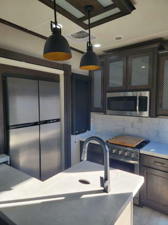 Modern RV rental kitchen featuring stainless appliances, island sink, stylish cabinetry, and pendant lights.. Grand Design Momentum 2022