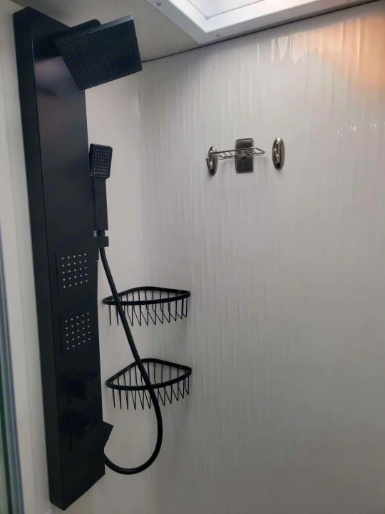 Modern RV rental shower with black panel offering rain, handheld & body jets, plus corner storage shelves.. Grand Design Momentum 2022