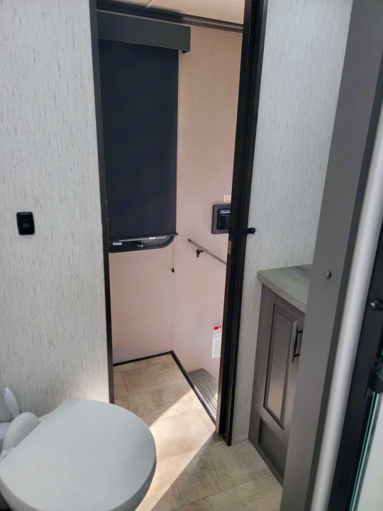 Inside an RV rental bathroom: features a modern toilet, vanity, and window blind, designed for efficient use of space.. Grand Design Momentum 2022