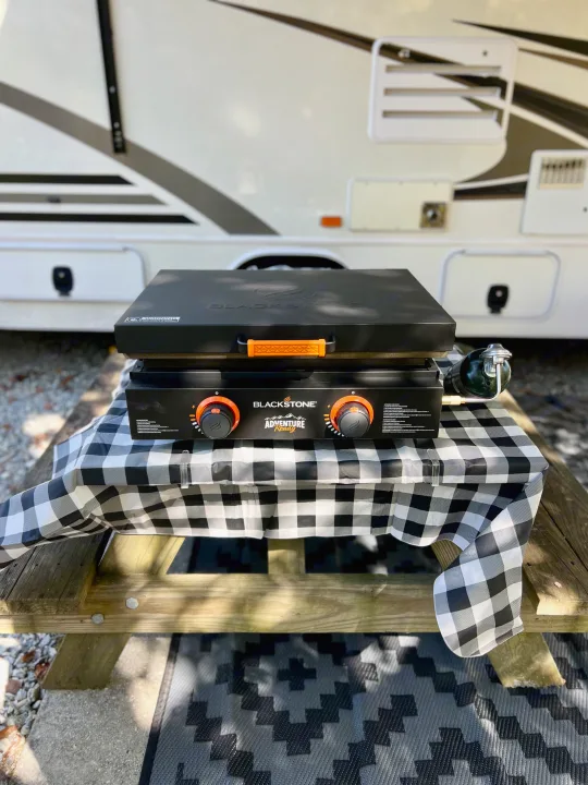RV rental trip! A Blackstone Adventure Ready griddle, covered, sits on a checkered picnic table for outdoor cooking.. Jayco Envoy 100 2018