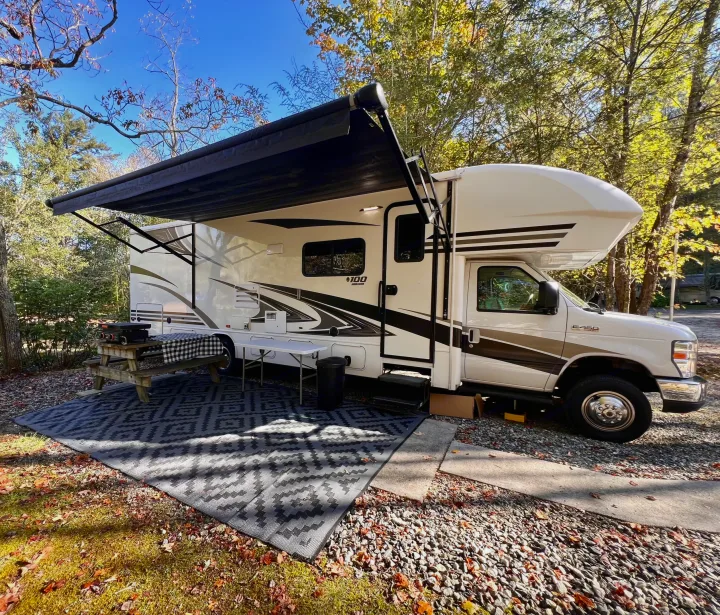 RV rental set up at a scenic campsite with awning, picnic table, and outdoor rug, perfect for a fall getaway.. Jayco Envoy 100 2018
