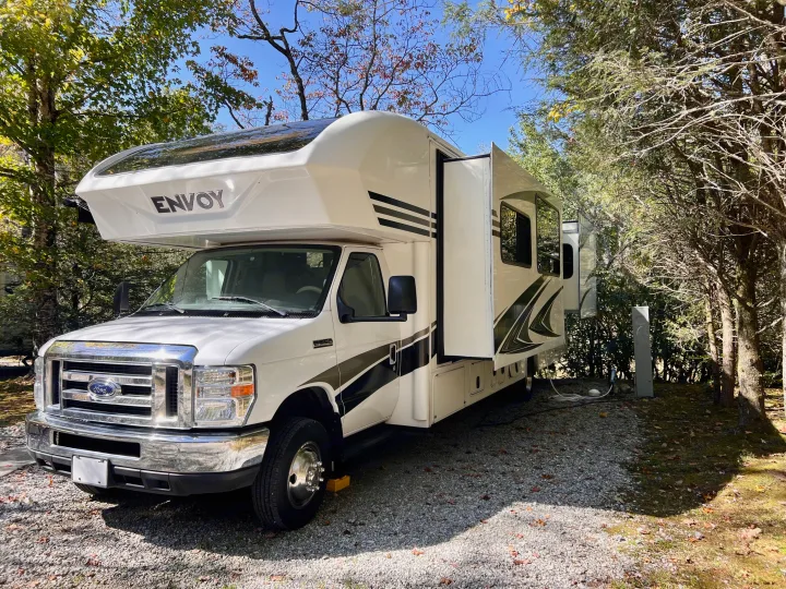 Spacious white Envoy RV rental parked at a serene gravel campsite with slide-out extended. Ready for your next trip!. Jayco Envoy 100 2018