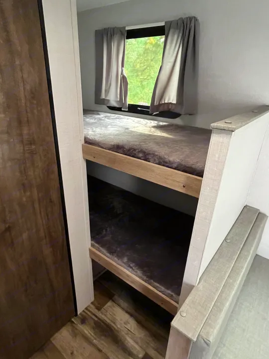 RV rental: Cozy bunk beds in a compact interior. A window above features gray curtains, an exit sign, and a view of trees.. Gulf Stream grand river 2024