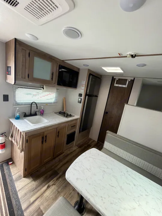 RV rental kitchen & dinette: modern wood cabinets, white counters, microwave, fridge, and comfy seating.. Gulf Stream grand river 2024