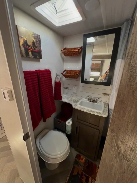 Functional RV rental bathroom featuring a compact sink, toilet, mirror, and smart storage, perfect for travel comfort.. Forest River Wildwood X-Lite 2020