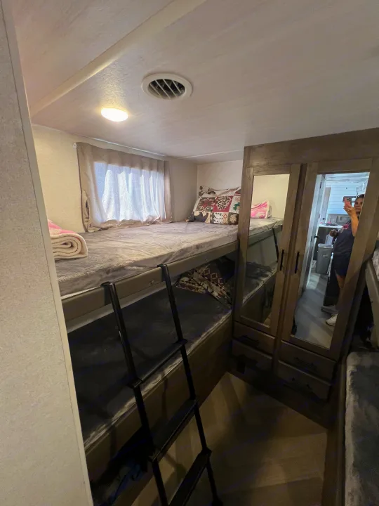 RV rental interior: Stacked bunk beds, window, ladder, and mirrored wardrobe for storage.. Forest River Wildwood X-Lite 2020