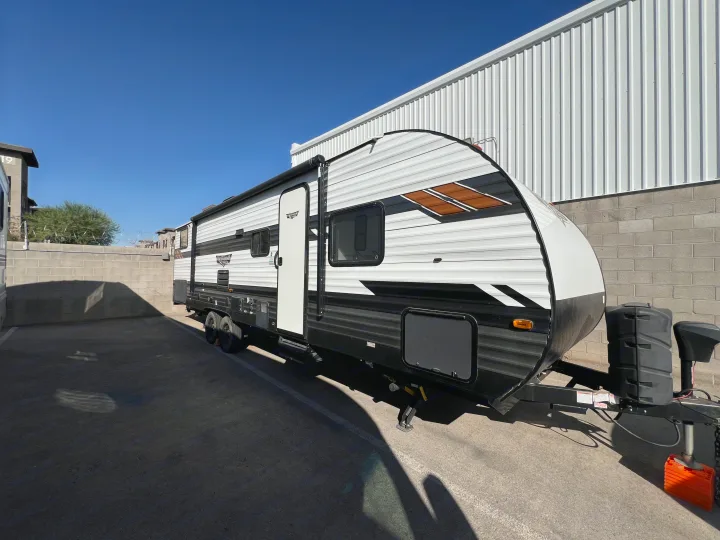 Sleek black, white, and brown travel trailer for rv rental, parked outdoors against a clear blue sky and white building.. Forest River Wildwood X-Lite 2020