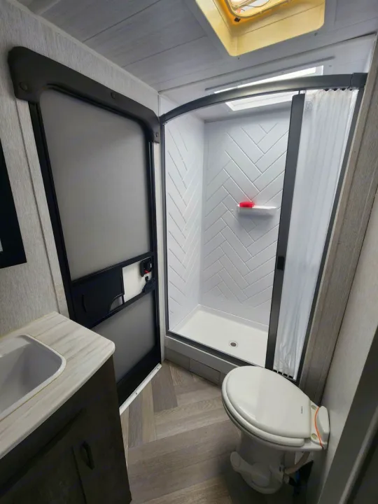 RV rental interior: A compact, modern bathroom with toilet, sink, and shower featuring elegant white herringbone tile.. Forest River Salem Cruise Lite 2022