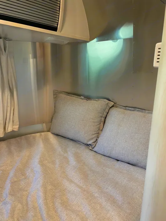 Cozy RV rental bed with light gray linen bedding and pillows, set within a sleek metallic travel trailer interior.. Airstream Bambi 2022