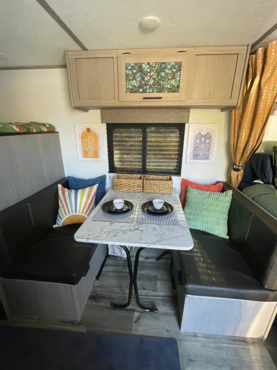 Cozy RV rental dinette with a marble table, booth seating, colorful pillows, and overhead storage.. Keystone RV COLEMAN LANTERN LT 17B 2024