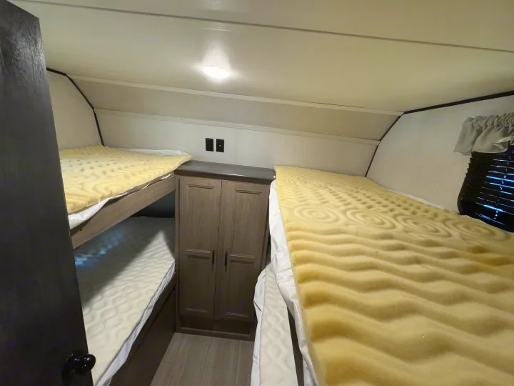 Cozy RV rental sleeping area featuring two bunk beds with yellow foam toppers and a central storage cabinet.. Keystone Hideout 2021
