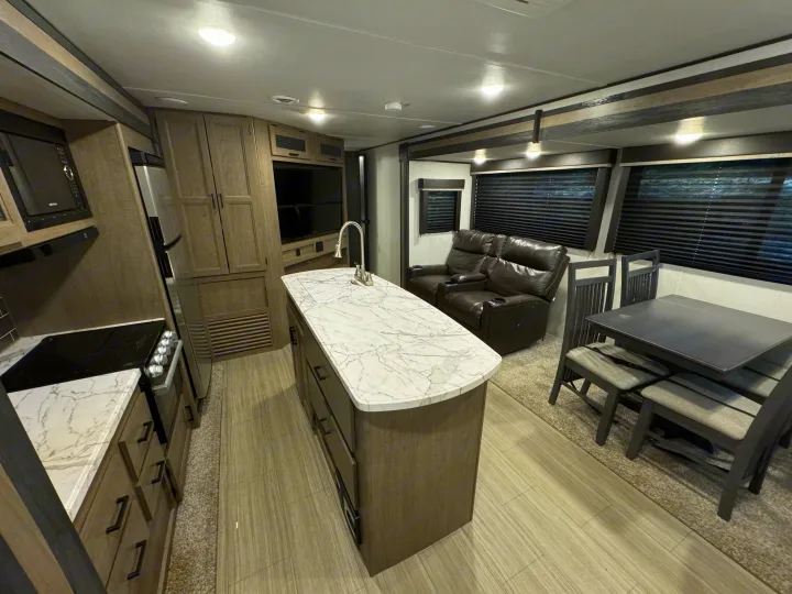 Explore this cozy RV rental interior featuring a full kitchen, island, recliner seating, and dining area.. Keystone Hideout 2021