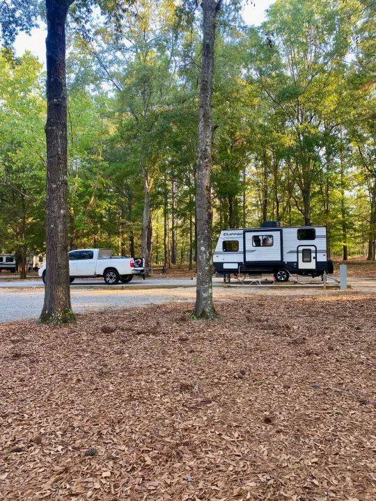 White Clipper RV rental and matching pickup truck parked on gravel at a treed campground. Fallen leaves cover the ground.. Clipper Clipper Trailer 2018