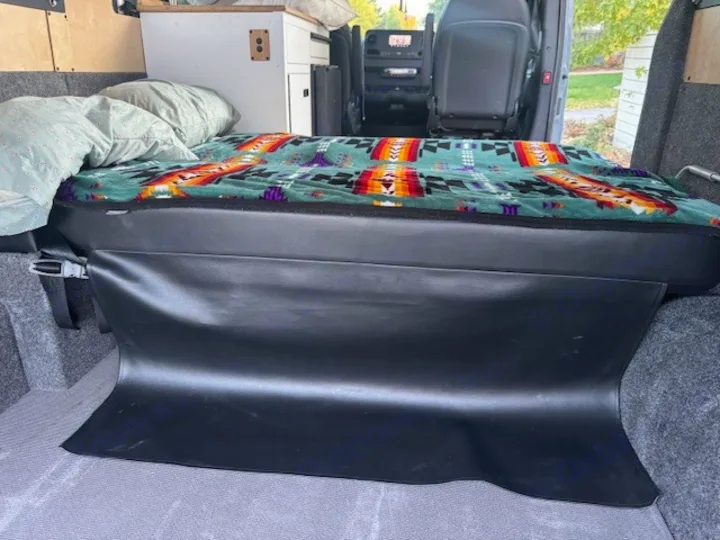 RV rental van interior: a custom bed with a vibrant patterned blanket, black skirting, and built-in storage for travel.. Mercedes-Benz Sprinter 2021