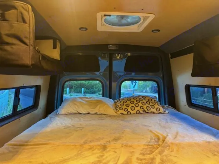 RV rental interior shows a bed with white sheets, side/rear windows, and overhead storage.. Mercedes-Benz Sprinter 2021