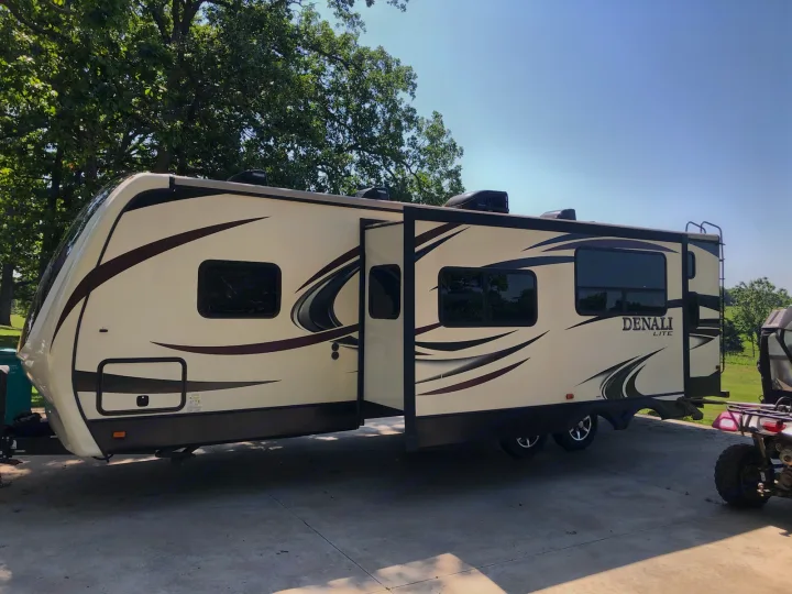 A cream-colored Denali Lite travel trailer RV with a slide-out extended is parked on concrete, ready for rv rental.. Denali Lite 2015