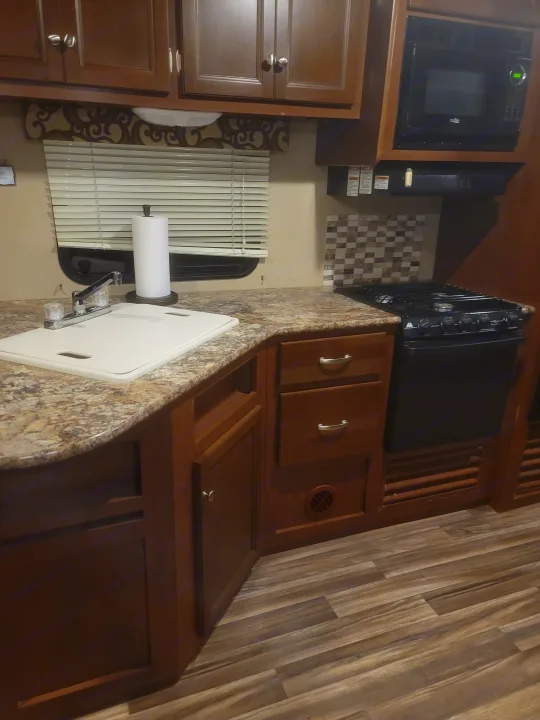 A clean, compact RV kitchen featuring a sink, microwave, stove, and wood cabinetry, ideal for an rv rental.. Denali Lite 2015