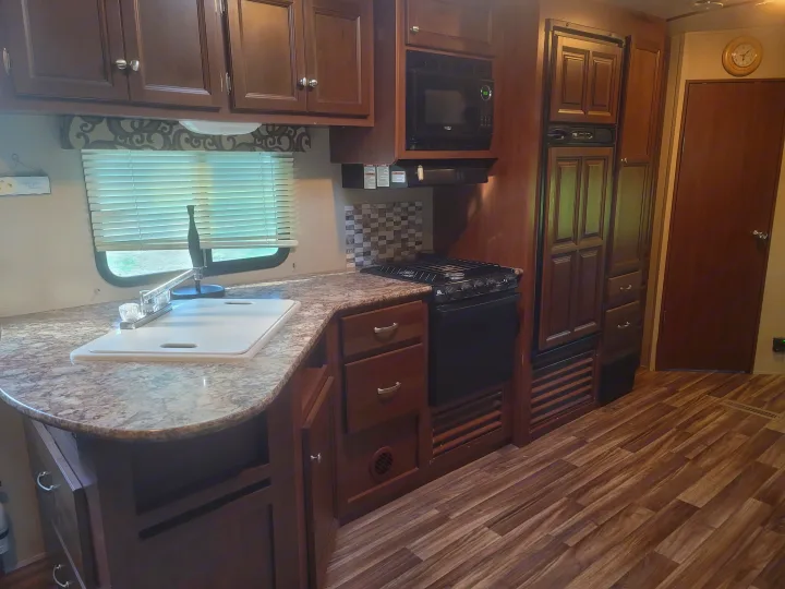 RV rental interior: A well-equipped kitchen with dark wood cabinets, sink, microwave, stove, and wood-look flooring.. Denali Lite 2015