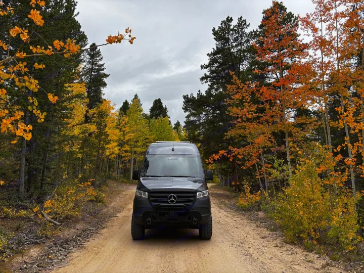 Black Mercedes Sprinter rv rental on a dirt road surrounded by vibrant yellow and orange fall foliage under a cloudy sky.. Mercedes Sprinter 2500 2024