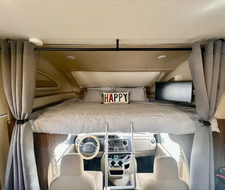 Spacious RV rental interior with a comfy cab-over bunk bed, TV, and Ford cockpit below.. Jayco Envoy 100 2018