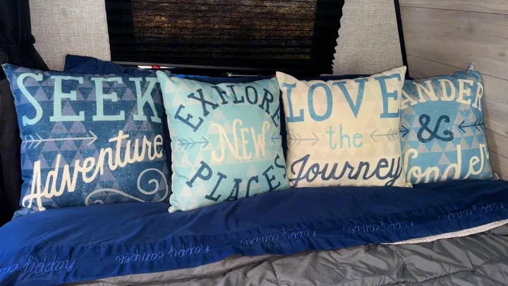 Cozy RV rental bed with adventure-themed pillows ("Seek Adventure," "Explore New Places") and a "happy camper" blanket.. Jayco Jay Flight SLX 2022