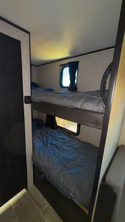 Inside an RV rental: two bunk beds with grey comforters, windows provide light. Perfect for family adventures.. Jayco Jay Flight SLX 2022