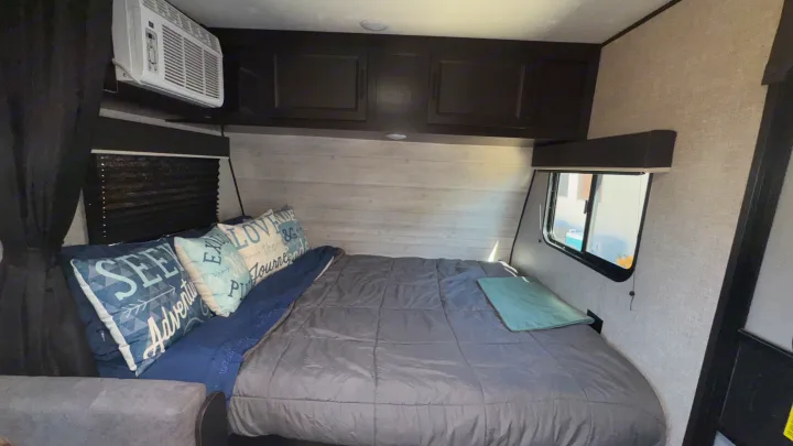Cozy RV rental bedroom: queen bed with decorative pillows, overhead storage, window AC, and blackout blinds.. Jayco Jay Flight SLX 2022