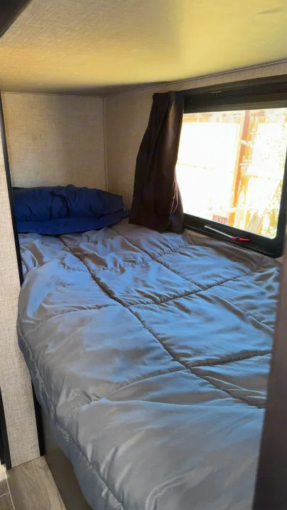 Comfortable RV rental sleeping area with a gray bed, blue pillow, and window showing an "EXIT" sign outside.. Jayco Jay Flight SLX 2022