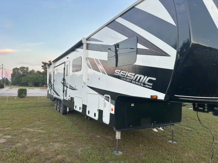 A large, white and black Jayco Seismic Luxury Series RV is parked on a grassy lot, a great option for rv rental.. Jayco Seismic 2023
