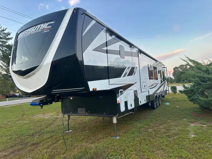 A large, black & white Jayco Seismic Luxury Series fifth-wheel RV, perfect for an RV rental, parked on green grass.. Jayco Seismic 2023