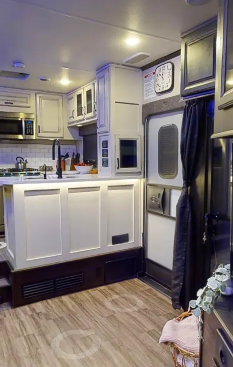 This modern RV rental kitchen features white cabinetry, a lighted island, and a main entry door, offering a comfortable travel space.. Jayco Seismic 2023