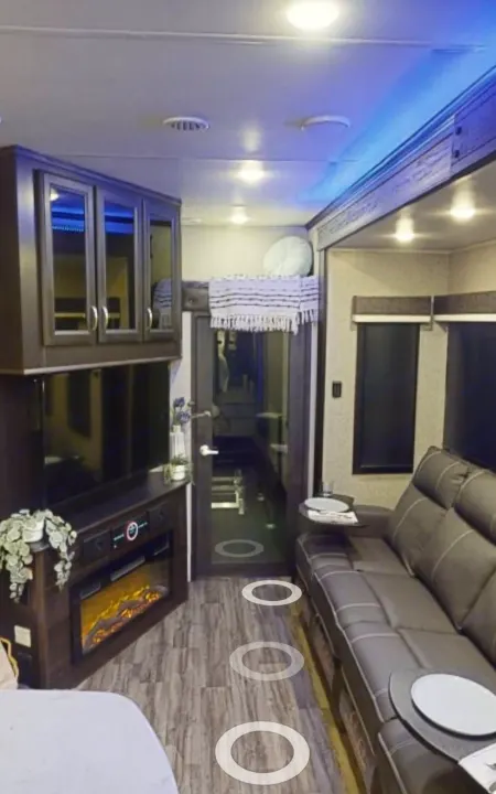 Explore this cozy RV rental interior: a modern living area with a dark grey couch, large TV, fireplace, and blue ceiling lights.. Jayco Seismic 2023