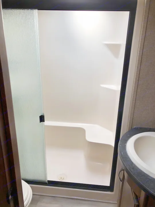 RV rental: Compact white shower with built-in seat, frosted door. Adjacent toilet and sink area shown.. Keystone RV Carbon Toy Hauler 2015