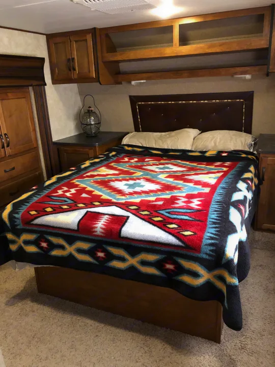 RV rental bedroom featuring a bed with a vibrant Southwestern-patterned blanket, brown headboard, and wooden cabinetry.. Keystone RV Carbon Toy Hauler 2015