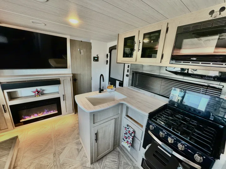 Discover this RV rental's bright interior! Features a compact kitchen, TV, electric fireplace, and cheerful Mickey Mouse accents.. Forest River Wildwood 2024